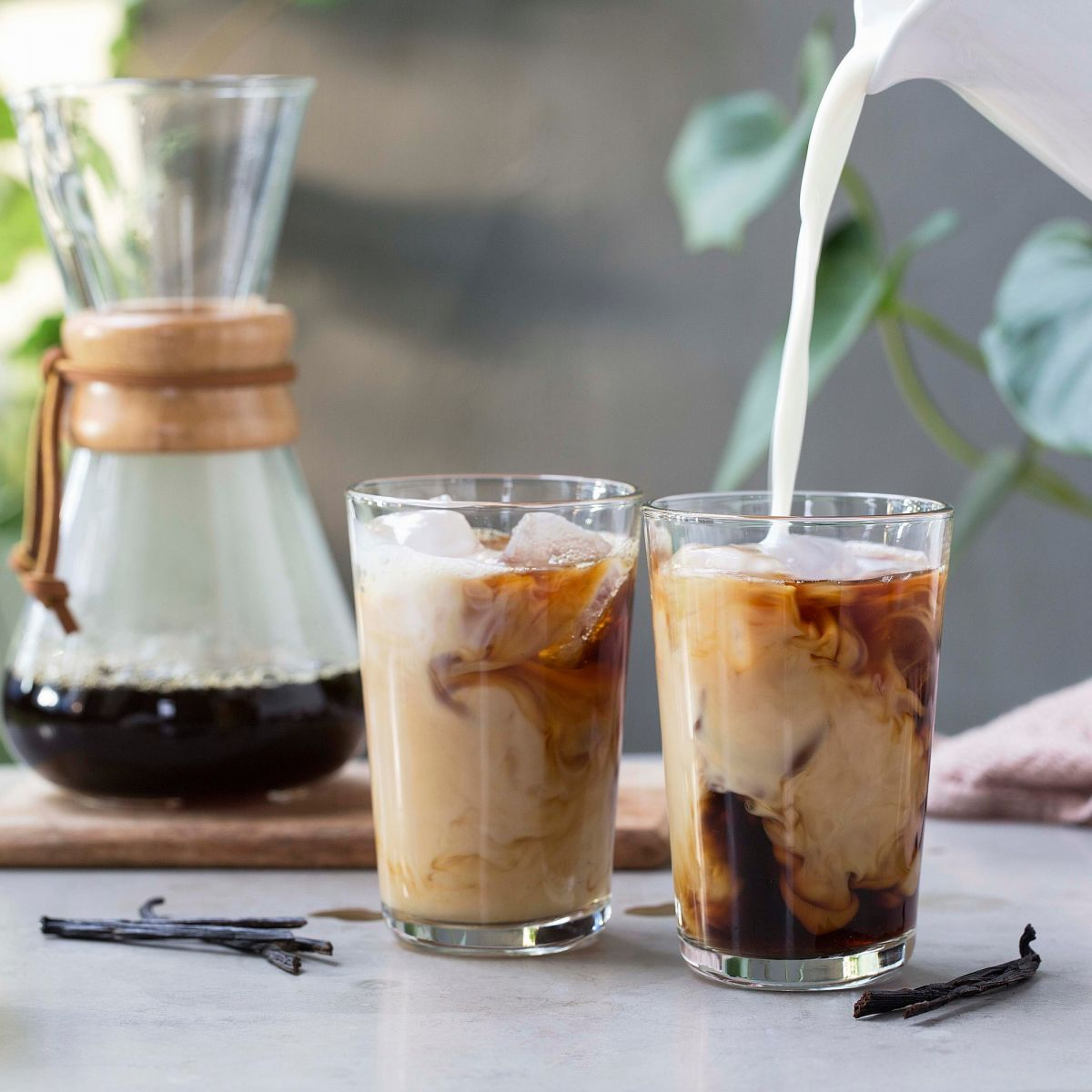Bildet viser to glass som står på en kjøkkenbenk. Glassene er fulle og inneholder kaffe, isbiter og melk. Kombinasjonen gjør at det er mønster i glasset. I det ene glasset helles det hvit melk fra toppen av bildet. Dette skaper et pent mønster i glasset, blant den mørke kaffen og isbitene.