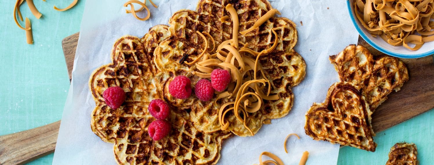 BIldet viser vafler liggende på et turkis bord med raspet brunost på toppen