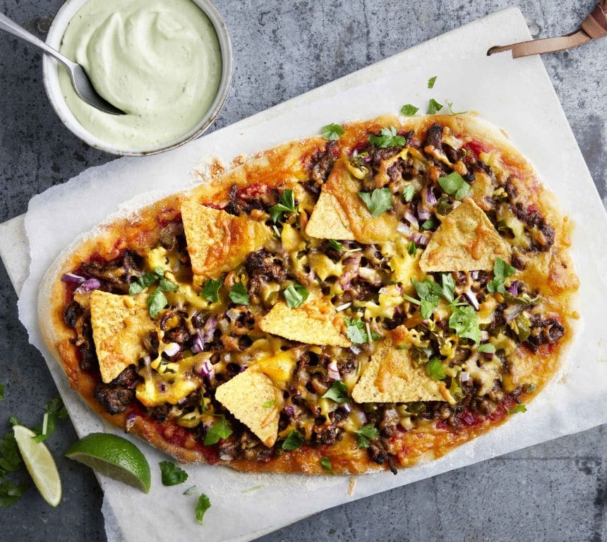 Pizza toppet med kjøttdeig og nachochips. Ved siden av står en skål med grønn avokadodressing.