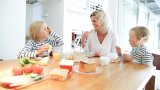 Mor og to barn samlet ved frokostbordet hjemme.