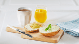 Rundstykke med kremost med kaffekopp og juice